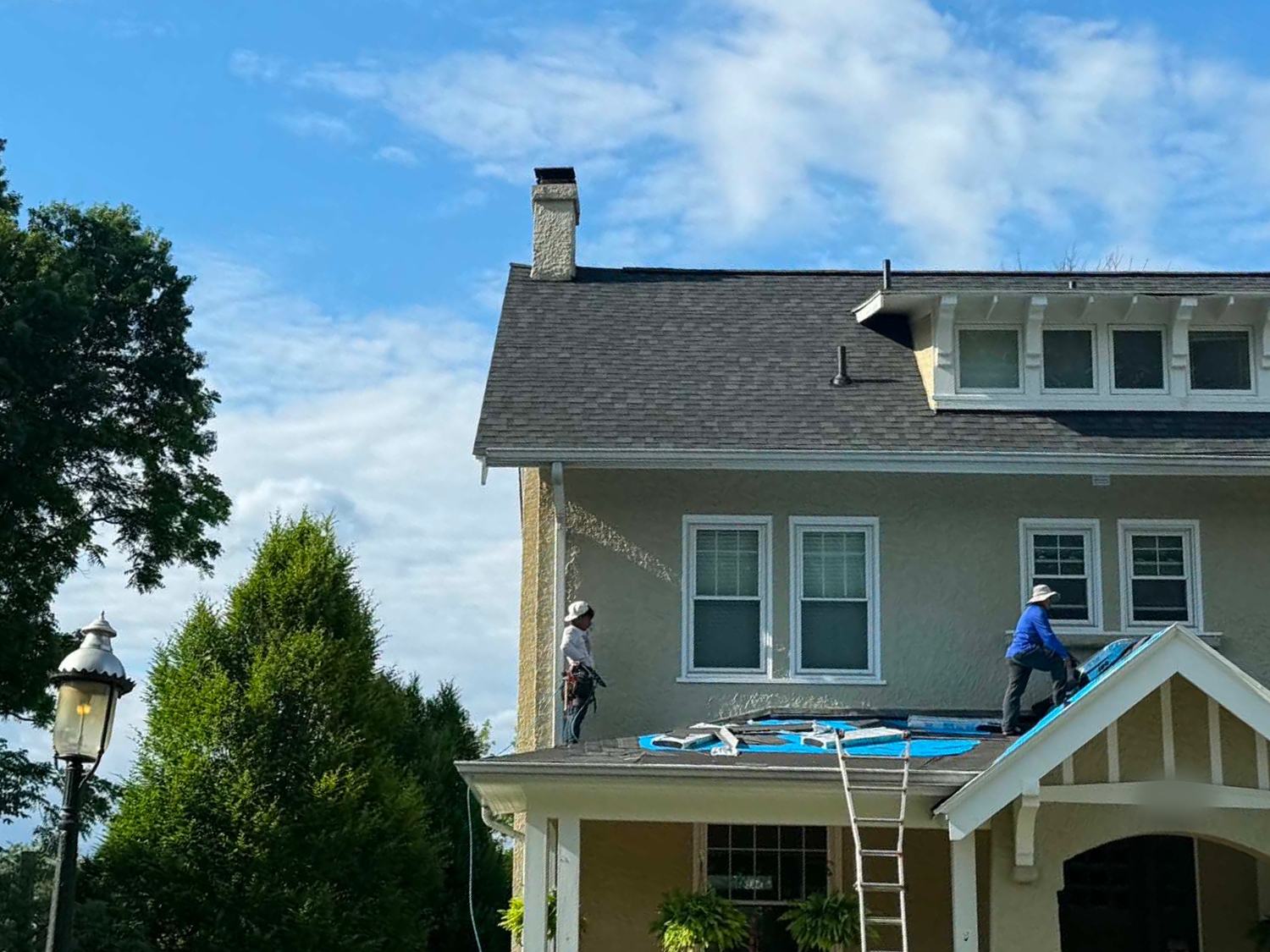 Crew laying ice-and-water shield across a front porch roof on an older stucco home