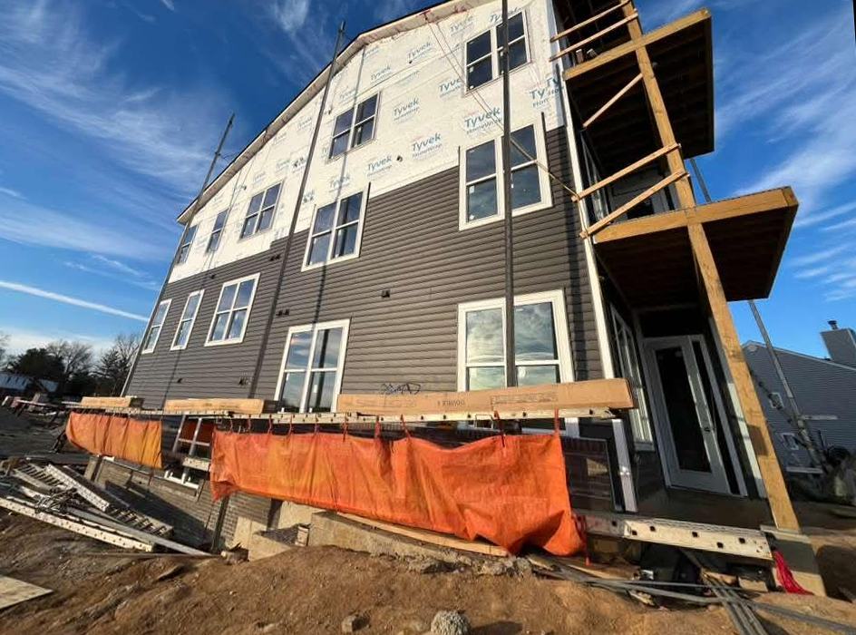 Dark siding being installed over housewrap on a three-story new build